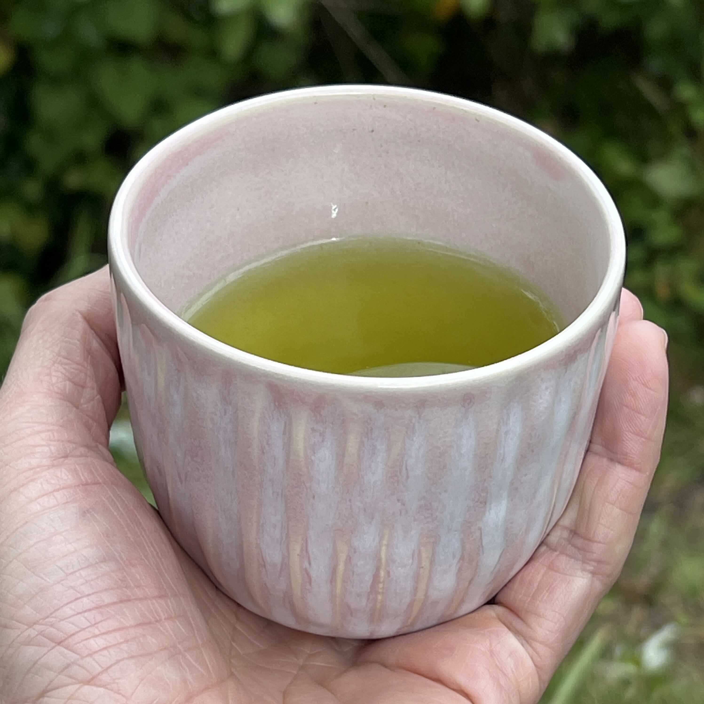 A hand holds a carved pink cup filled with green tea.