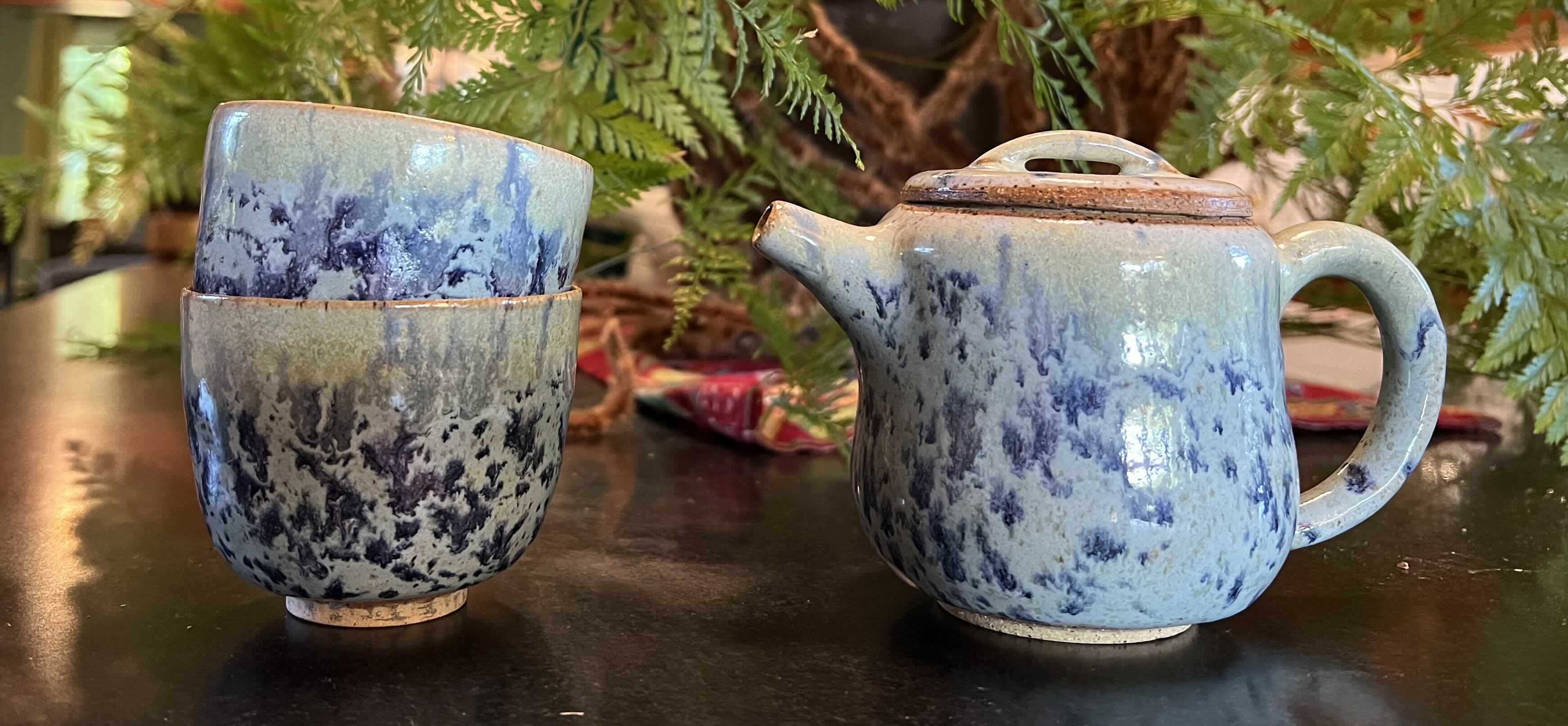 Two teacups and a teapot. The glaze swirls like the sea.