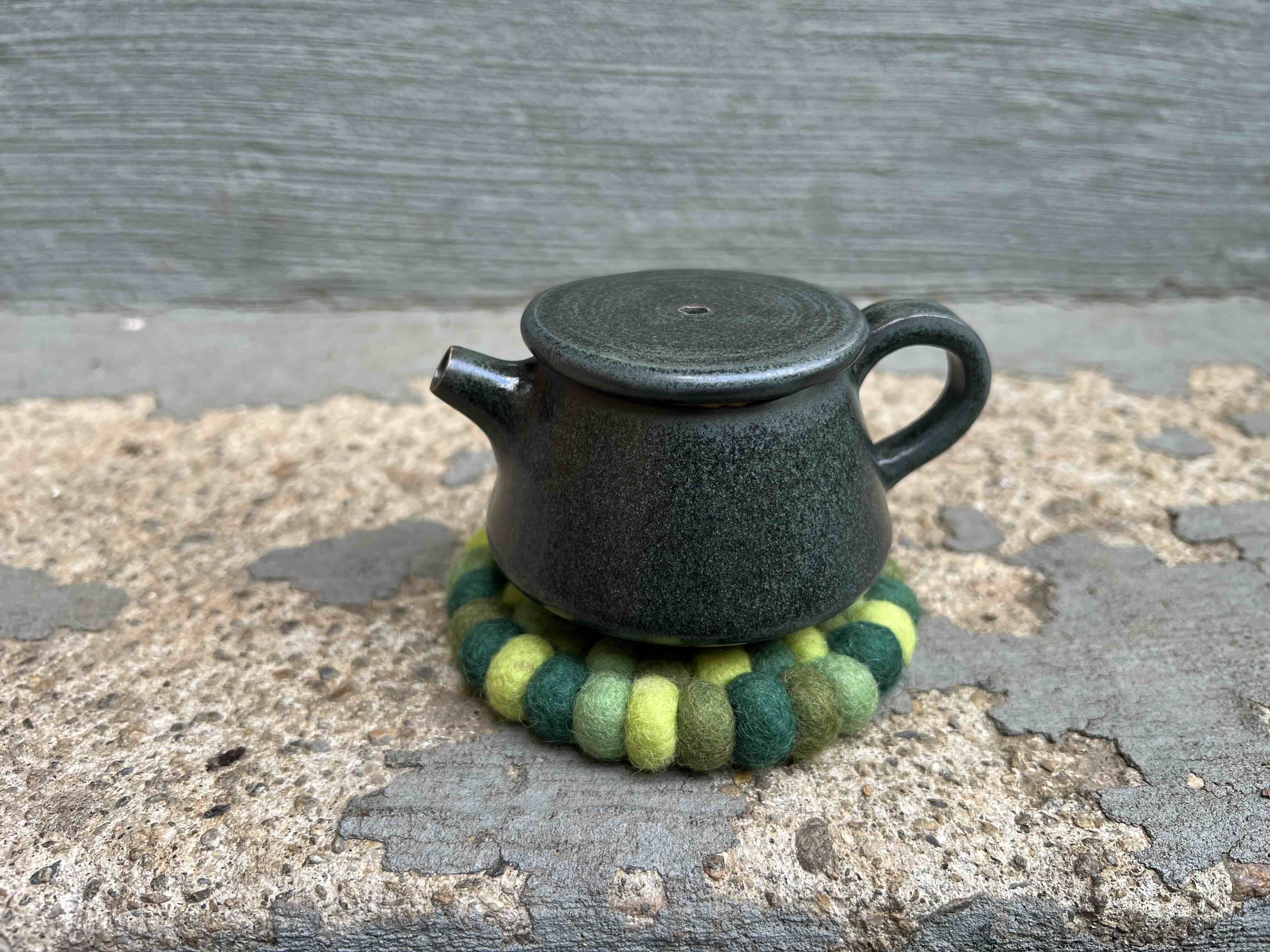 A small black teapot on a fancy coaster.